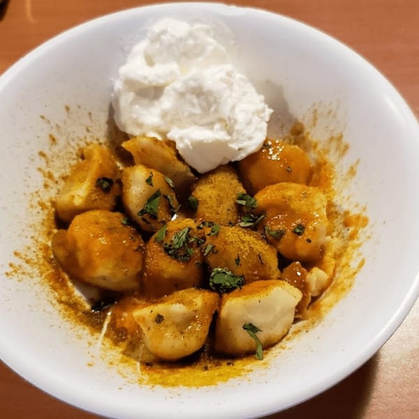 Pel Meni Dumpling Tzar dumplings with sauce, spices, and a dollop of sour cream.