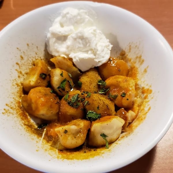 Pel Meni Dumpling Tzar's dumplings with a savory sauce, spices, and a dollop of sour cream.