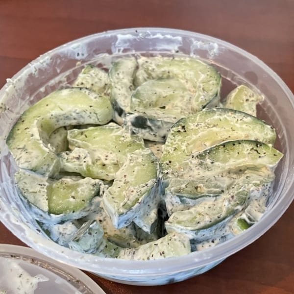 Cucumber salad with creamy dressing and dill in a clear plastic container from Pel Meni Dumpling Tzar.