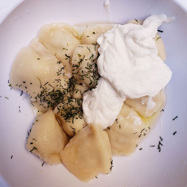 Pel Meni dumplings with sour cream and dill in a white bowl.