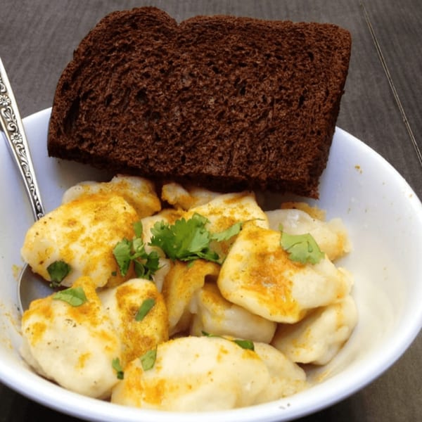 A white bowl of Pel Meni dumplings topped with spices and cilantro, served with dark bread.